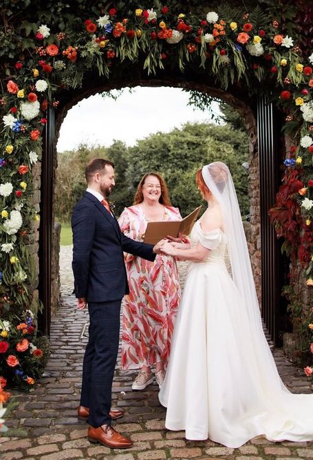 Bride and Groom smiling, with the backdrop of an arch of flowers behind them.